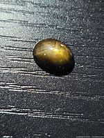 Loose oval cabochon star sapphire on textured surface showing body color and dome