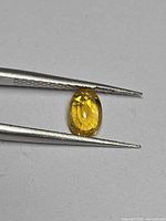 Front view of oval yellow sapphire held by tweezers