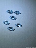 Six pear-cut sky blue topaz gemstones displayed on neutral background