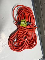 Full view of coiled orange extension cord with green tape marker showing male and female ends
