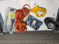 All five items laid out: orange extension cord, yellow adapter cord, Top Wallet package, Bell+Howell flashlight, hobby knife set in clear case