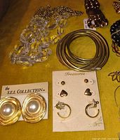 Group shot showing clear bead necklace, stack of gold-tone bangles, faux pearl earrings on S.E.I. Collection card and earring set on Treasures card
