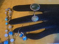 Black velvet display hand showing two silver-tone rings with green cabochons, portion of beaded strand and single blue bead earring
