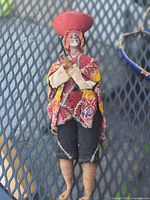Textile folk doll wearing multicoloured woven poncho, black trousers, red round hat