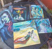 All six paintings laid on round metal table showing variety of subjects