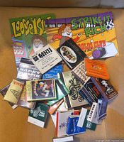 Pile of colorful advertising matchbooks and two promo cards displayed on surface