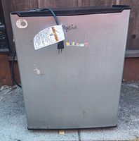 Front view showing stainless-look door with stickers and power cord