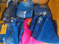 Six folded pairs of jeans, five blue one pink, tags visible