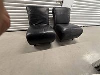 Front view of the two matching black leather armless lounge chairs