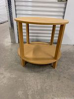 Angle view of round wood side table showing top, legs, and lower shelf