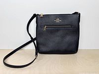 Front view of black Coach Rowan File Bag with strap and front zip pocket visible
