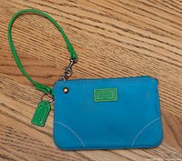 Front view of blue and green Coach wristlet showing strap, hang tag and overall condition
