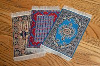 Three miniature woven rugs overlapped showing patterns and fringe
