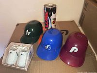Lot overview showing three helmets, Coca-Cola can, boxed baby shoe shakers