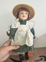Front view of porcelain doll on stand with straw hat, apron, green dress