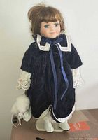 Front view of porcelain doll in navy velvet outfit on stand holding skates