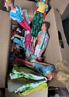Box containing three Barbie dolls, one Ken doll and jumble of clothes/accessories