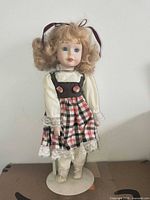 Front view of porcelain doll on stand in plaid dress