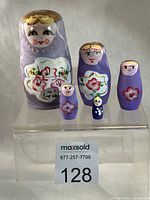 Front view of all five lavender nesting dolls showing painted faces and floral designs