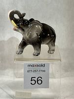 Front left view of glossy grey porcelain elephant on clear stand