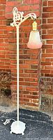 Full view of white wrought iron bridge floor lamp against brick wall