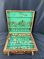 Open wooden case showing organized brass flatware and serving pieces