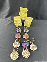 Nine cloisonné tape measures with keyrings arranged in rows with six yellow patterned boxes behind