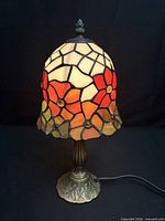 Lamp illuminated showing multi-coloured floral stained glass shade and bronze-tone base