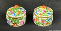 Two round porcelain lidded boxes showing floral pattern and strawberry finials