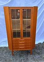Front view of teak corner cabinet showing glass doors, drawers and overall design