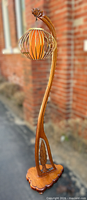 Full view of sculptural teak floor lamp showing curved body, wire cage shade, and base