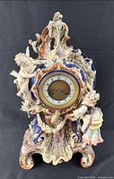 Front view showing complete porcelain mantel clock, cherubs, florals and dial