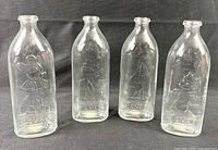 Front view of four clear glass Comfy baby bottles showing embossed characters and logos