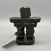 rear view of black stone inukshuk figurine, leather cord and tag visible