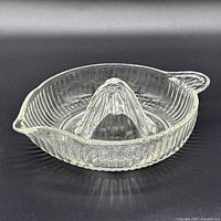 Side view of clear glass citrus juicer showing ribbed bowl, reamer cone, spout and handle