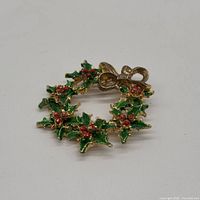 Front view of gold-tone enamel holly wreath brooch showing green leaves, red berries, gold bow