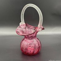 Front view of cranberry pink glass basket vase showing ruffled rim and clear applied handle