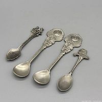 Four pewter souvenir teaspoons side by side