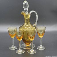 Front view of amber glass decanter with stopper and four stemmed glasses