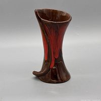 Front view shows brown body with red drip glaze and curved accent at base