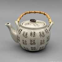 Full view of porcelain teapot showing bamboo handle and Asian character decoration
