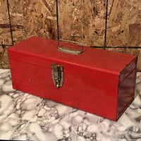 Angled view of red metal toolbox showing latch, handle and wear