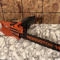 Full view of Remington orange and black corded chainsaw on work surface