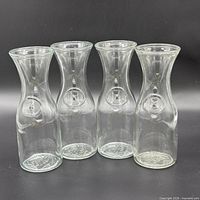 Front view of four clear glass carafes showing overall shape and embossed medallions