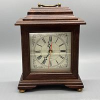 Front view showing entire clock face, wood case, brass handle and feet