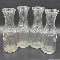 Four clear glass Libbey carafes front view showing embossed medallion and grape base