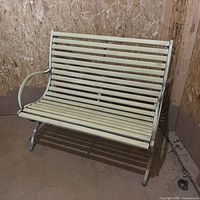 Front angled view of cream metal slatted bench showing armrest and legs