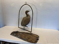 Full view of peacock sculpture in hanging frame with detached tail on table