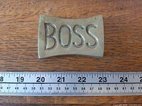 Top view of brass “BOSS” paperweight with ruler showing length