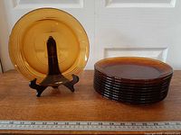 Stack of 11 amber Duralex Ondine plates and one plate on stand